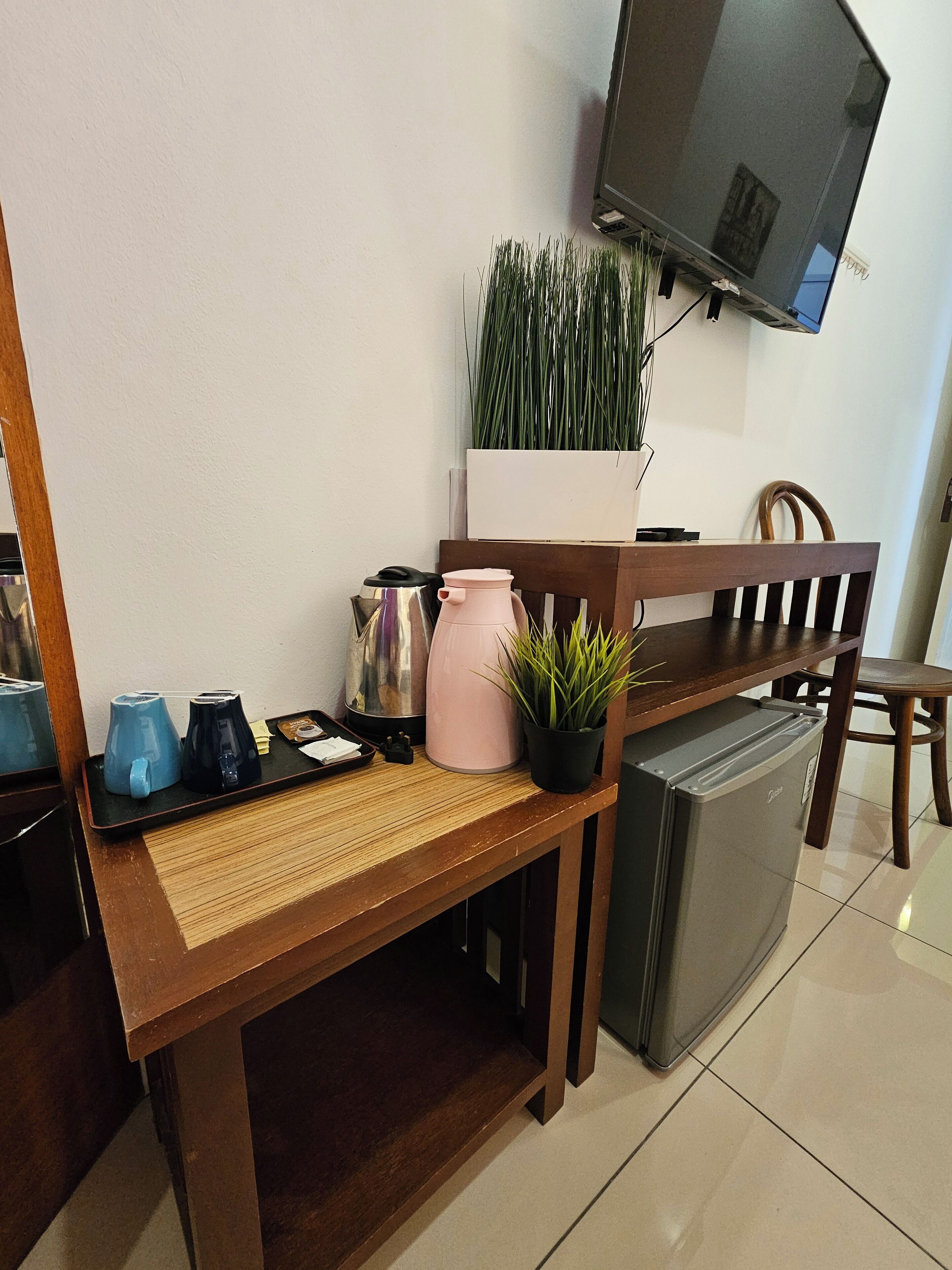 Een kitchenette met een koffiezetapparaat, een broodrooster, een waterkoker, een kleine koelkast, een potplant en een aan de muur bevestigde televisie.