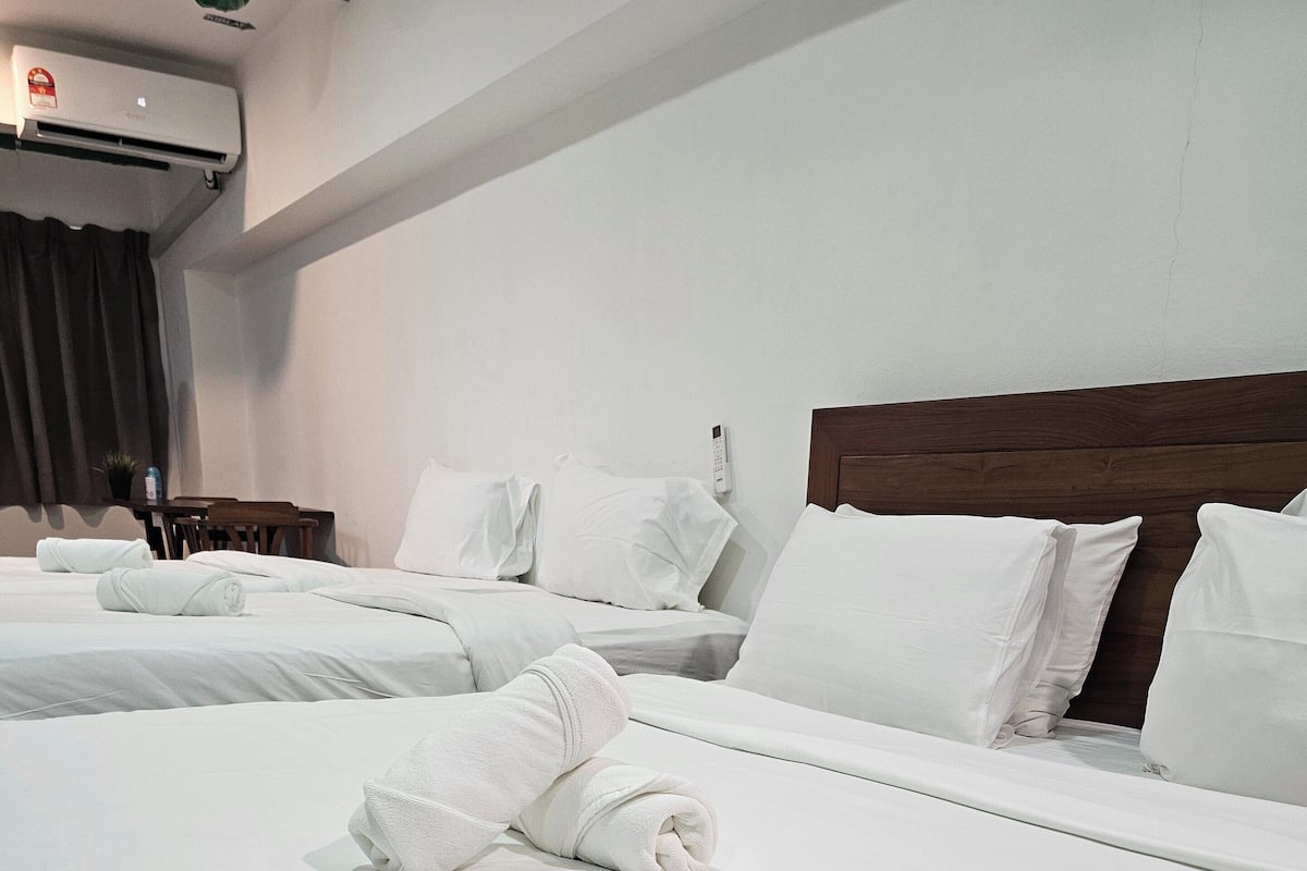 A hotel room with two beds, white linens, a wooden headboard, a bedside table, a remote control, and a potted plant.