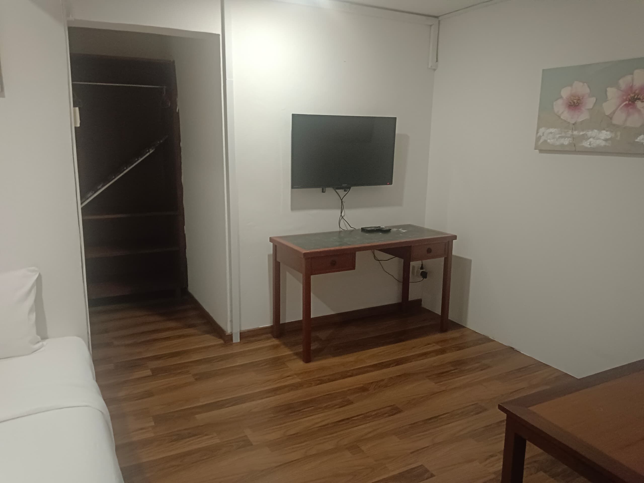 Une pièce avec un bureau en bois, un téléviseur fixé au mur, un canapé blanc et un plancher en bois.