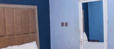 Un dormitorio con cama, cabecera, puerta y toma de corriente.