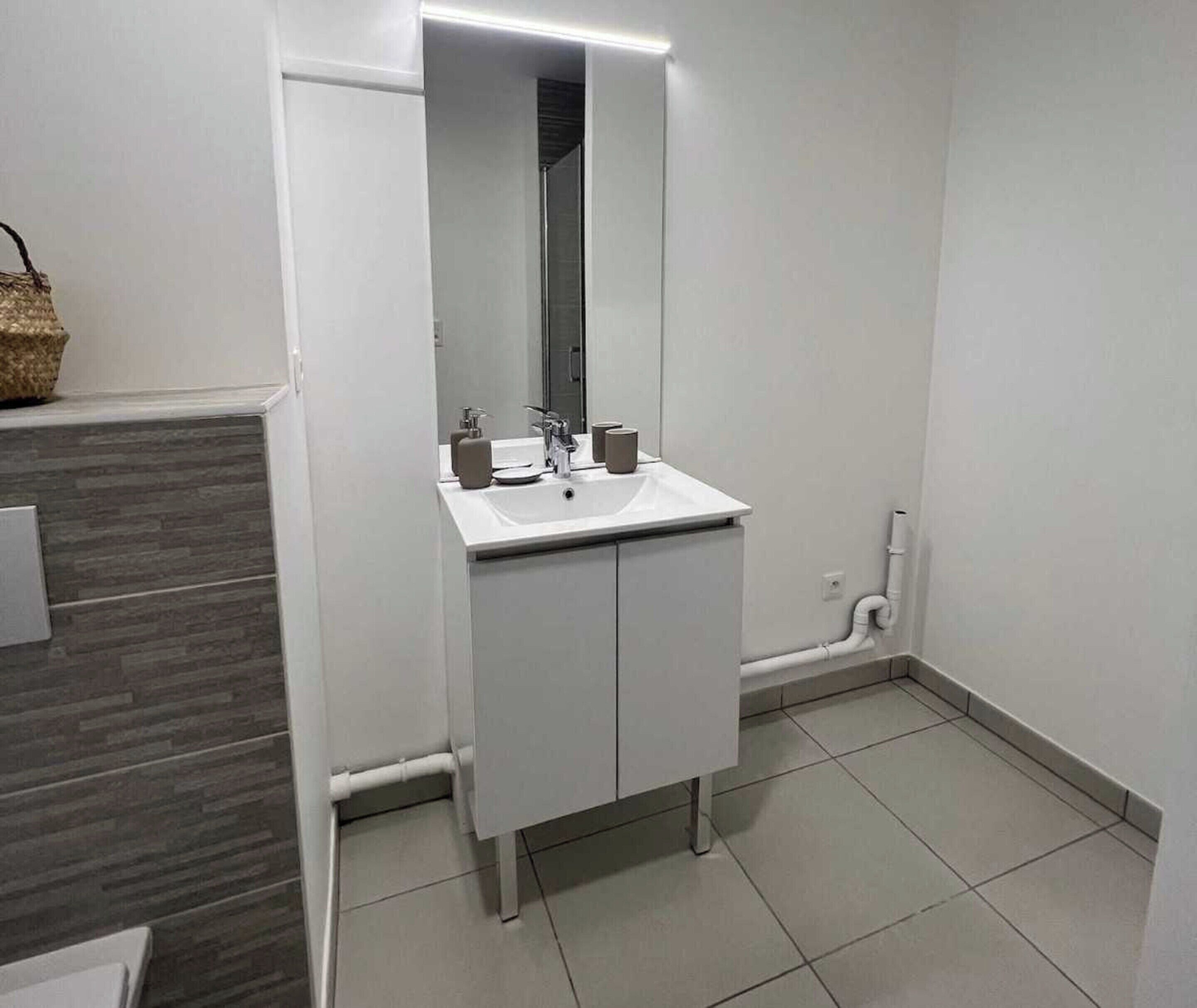 Een moderne badkamer met een witte wastafel, spiegel en kast.