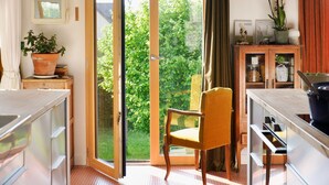 A kitchen with a sliding glass door leading to a balcony, a wooden chair, and a small cabinet with a potted plant.