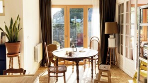 A dining area with a round table, chairs, a potted plant, a lamp, and a view through a glass door.