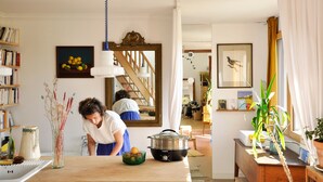 A kitchen with a stove, sink, and a window with curtains. There is a mirror above the sink and a bookshelf with books.