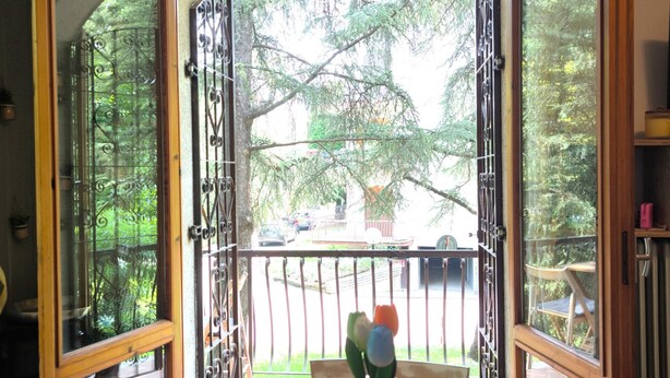 Puerta abierta que da a un balcón con una mesa de madera y un florero.