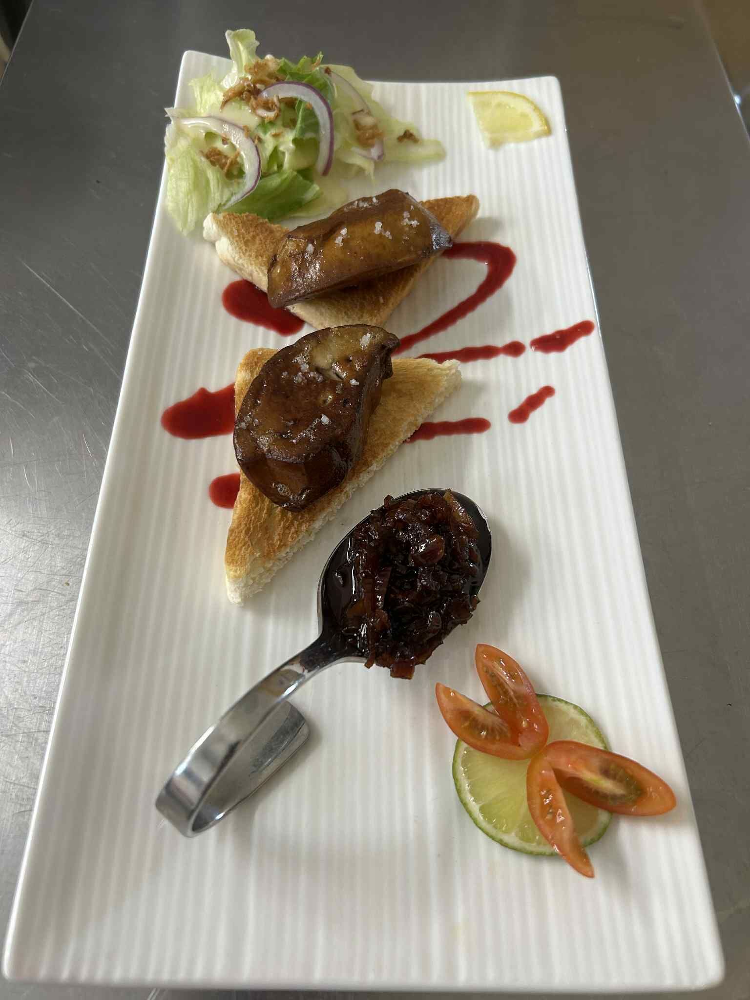 Une assiette rectangulaire blanche contenant une salade, deux morceaux de pain nappés d’une sauce brune et une cuillère de condiment foncé.