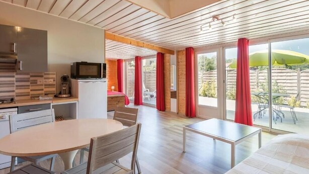 Una habitación de hotel moderna con cocina, comedor y balcón con cortinas rojas.