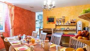 Un comedor con una mesa de madera dispuesta para el desayuno, una araña y una cesta de frutas.