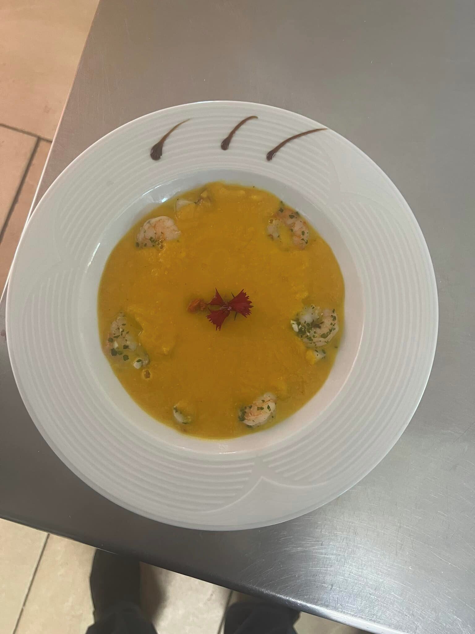 A white bowl of soup with shrimp and a garnish on a table.