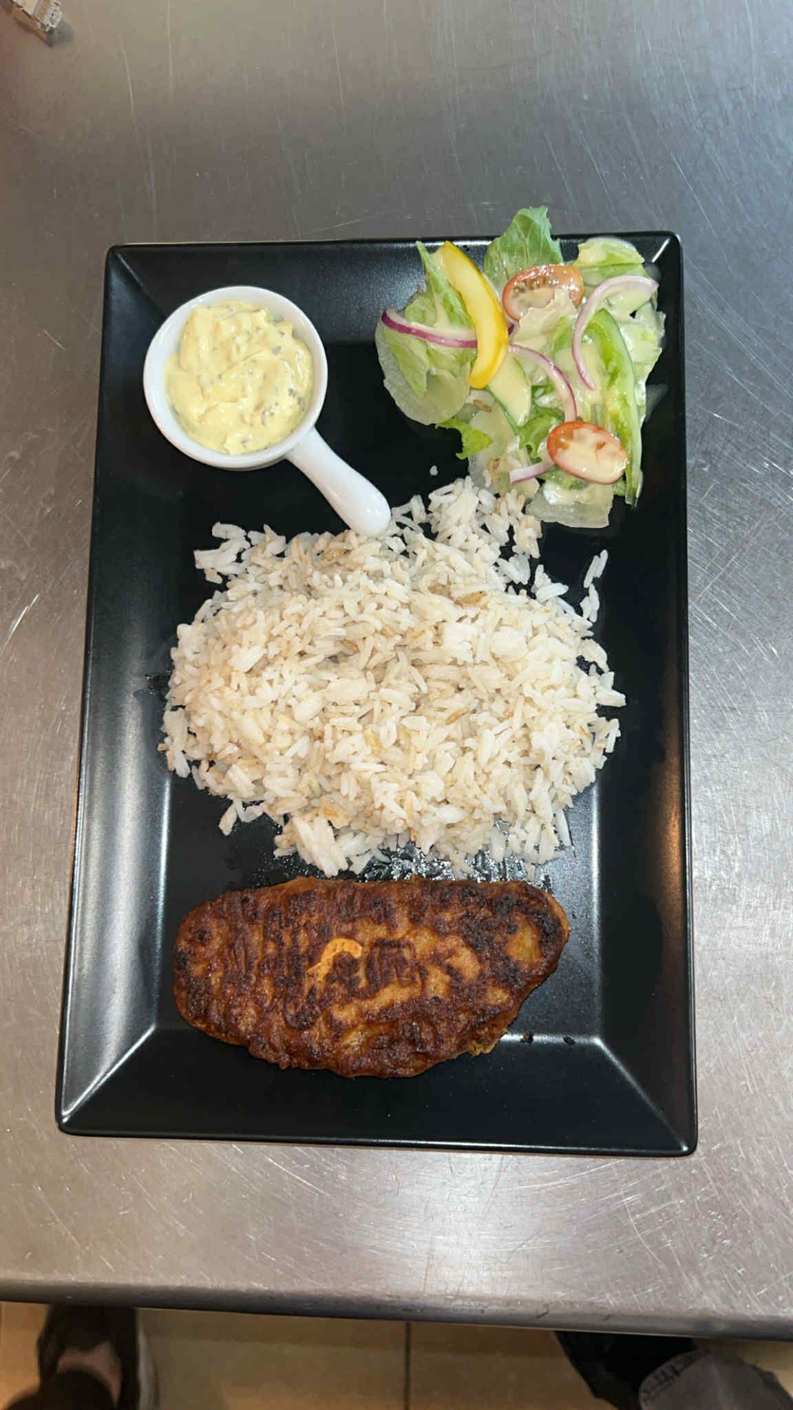 A plate with rice, a grilled meat, a salad, and a small bowl of sauce.