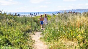 Een pad dat naar een strand leidt, met mensen op de achtergrond.