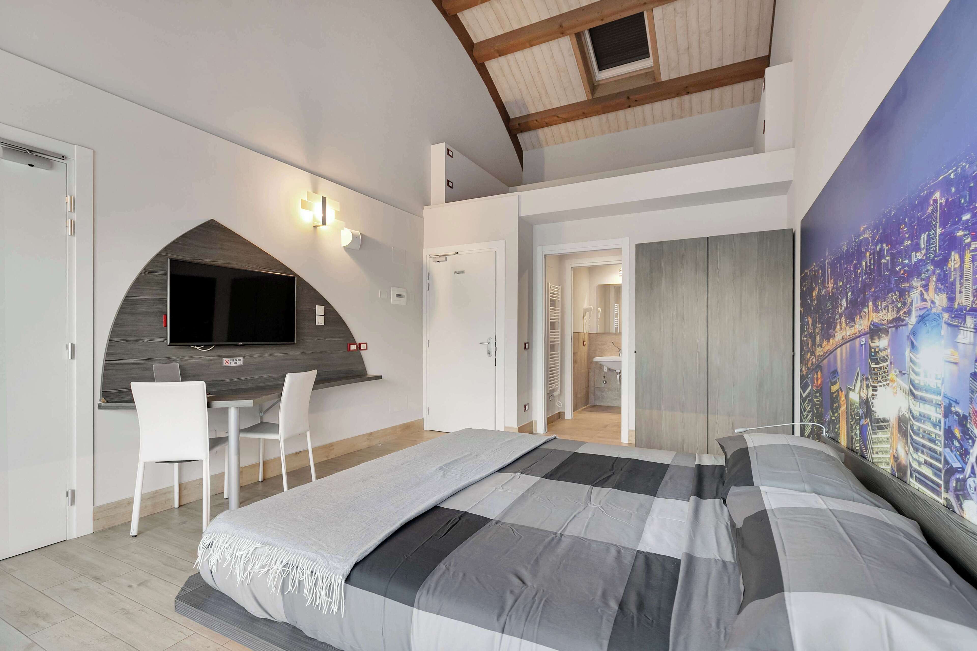 A modern bedroom with a bed, a desk, and a TV.