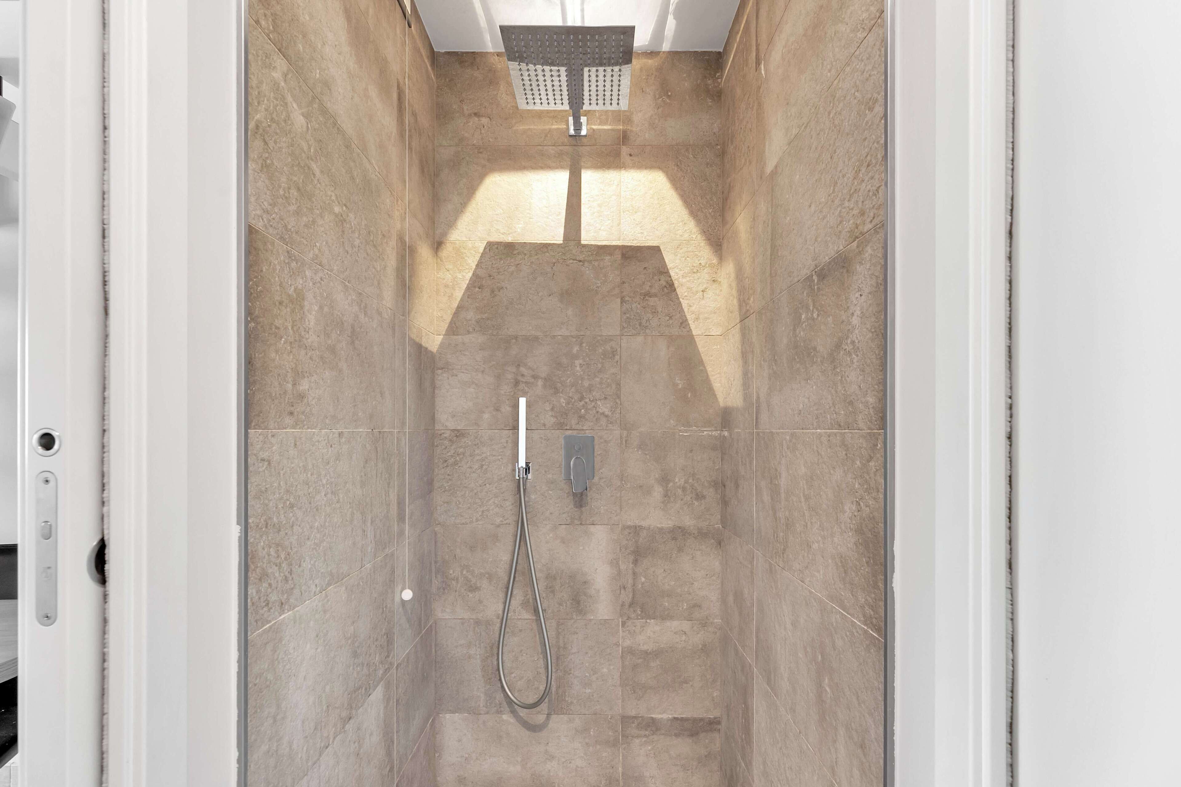 A shower with a handheld showerhead and a wall-mounted control panel.