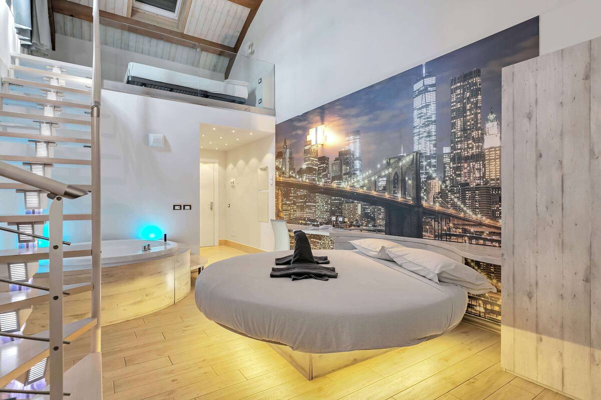 A bedroom with a cityscape mural, a round bed, a staircase, and a built-in bench.