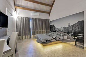 Une chambre moderne avec un lit aux lignes courbes, un téléviseur à écran plat, un coin repas et une grande fresque murale représentant un paysage urbain.