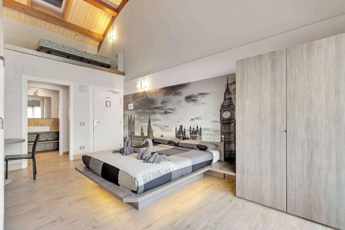 A modern bedroom with a bed, a desk, and a wardrobe. There is a mural of a city skyline on the wall.