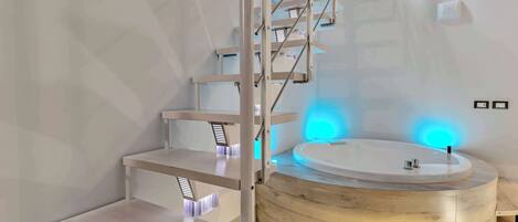 A modern bathroom with a freestanding bathtub, a wooden vanity, and a staircase with integrated lighting.