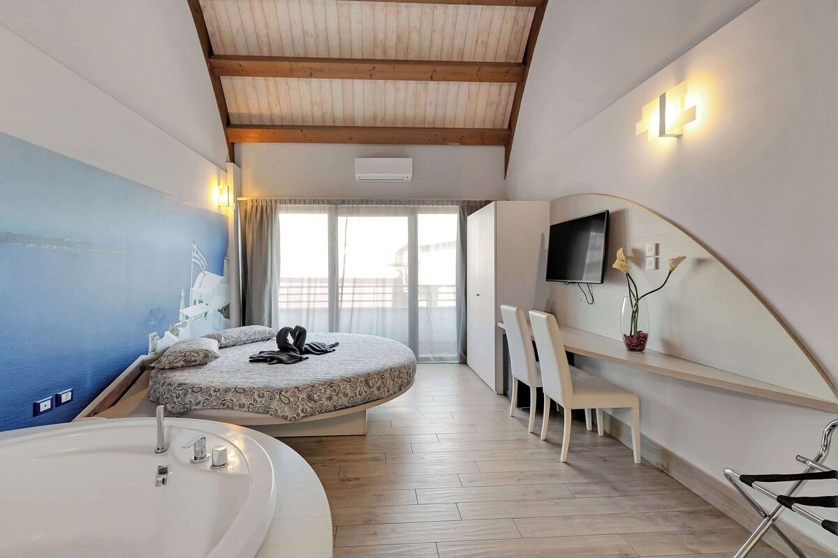 Une chambre à coucher moderne avec un lit aux lignes courbes, une grande fenêtre, un téléviseur et un espace bureau.