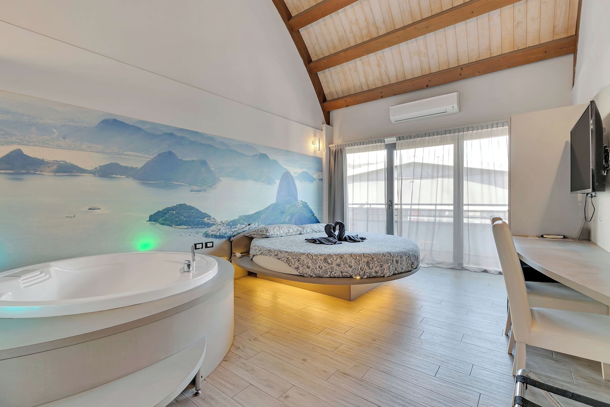 Une chambre à coucher moderne avec un grand lit, une baignoire et une fresque murale représentant un paysage.