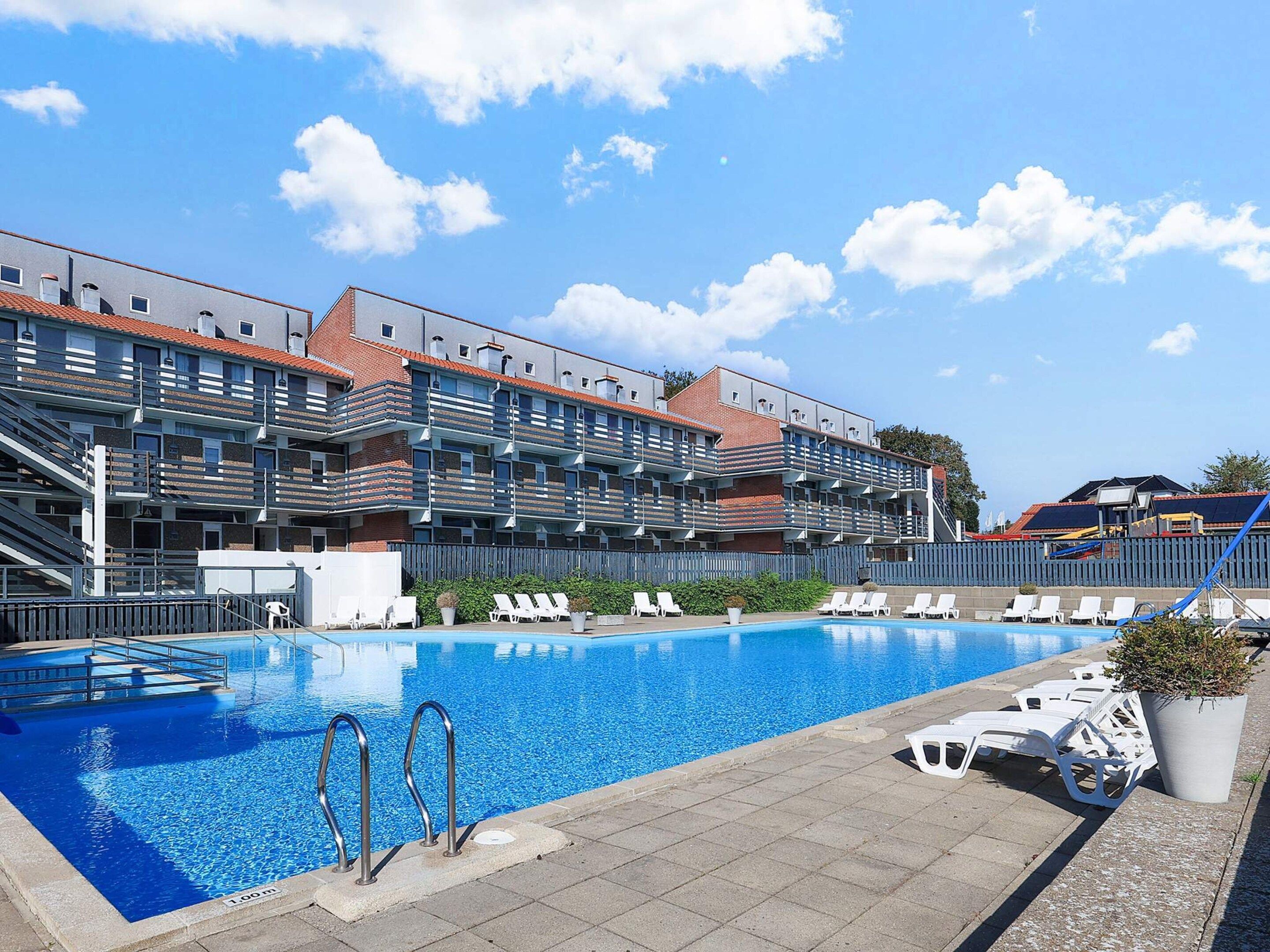 A swimming pool with lounge chairs and a building with multiple balconies in the background.