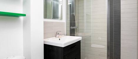 A modern bathroom with a white sink, black vanity, and a glass shower enclosure.