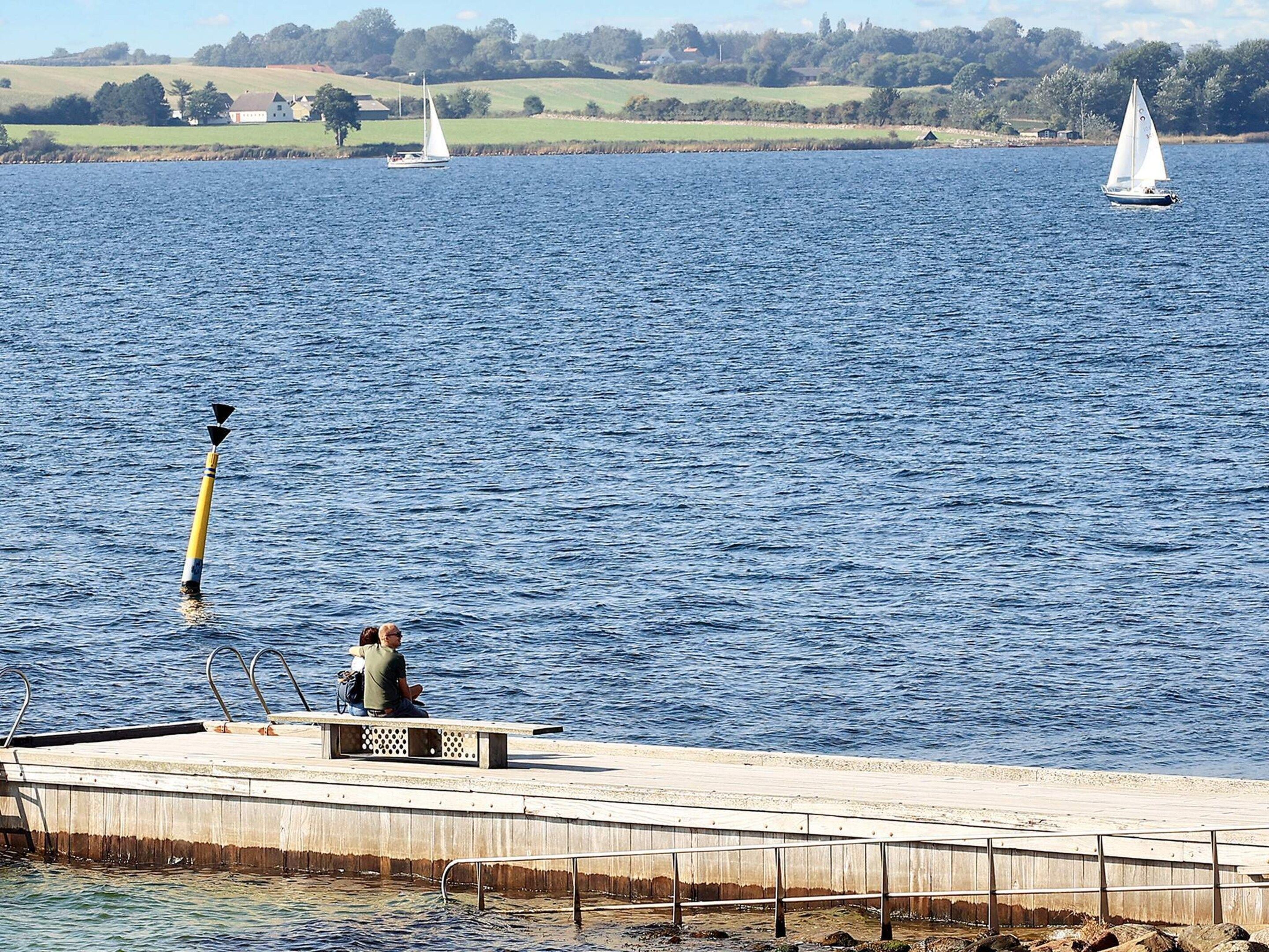 A pier extending into a calm body of water with a sailboat in the distance.