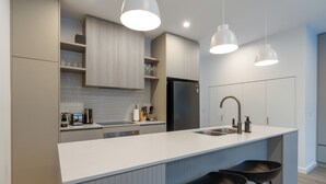 Eine moderne Küche mit Kochinsel, Barhocker, Kühlschrank und Pendelleuchten.