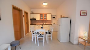 Uma cozinha compacta com armários brancos, uma geladeira branca e uma mesa de jantar com cadeiras.