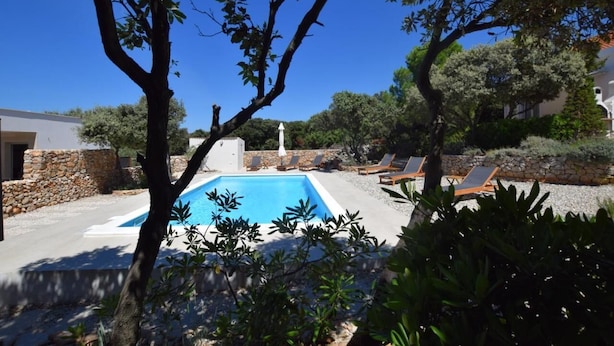 Piscina com espreguiçadeiras e um muro de pedra.