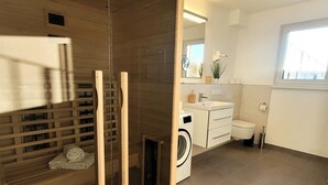 A modern bathroom with a glass shower enclosure, a built-in washing machine, a toilet, and a sink with a mirror above it. - Winterberg Apartment Near ski Area (Winterberg)