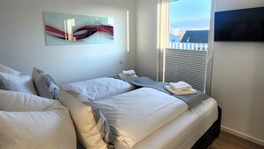 A modern bedroom with a large bed, a flat-screen TV mounted on the wall, and a window with blinds. - Winterberg Apartment Near ski Area (Winterberg)