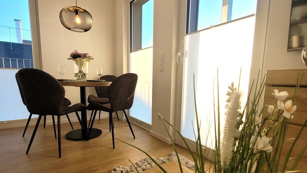 A dining area with a round table and four chairs, a hanging light fixture, and a view of the outside through large windows. - Winterberg Apartment Near ski Area (Winterberg)