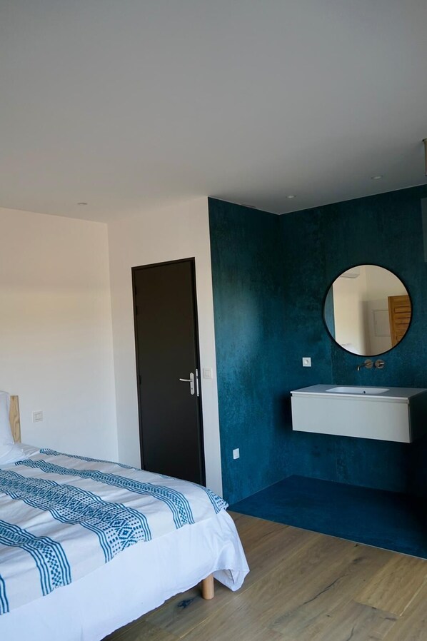 A bedroom with a bed, a dark door, a blue accent wall, a round mirror, and a white sink.