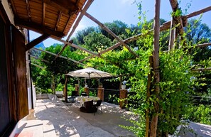 An outdoor patio with a table and chairs, a pergola, and a view of the surrounding greenery.