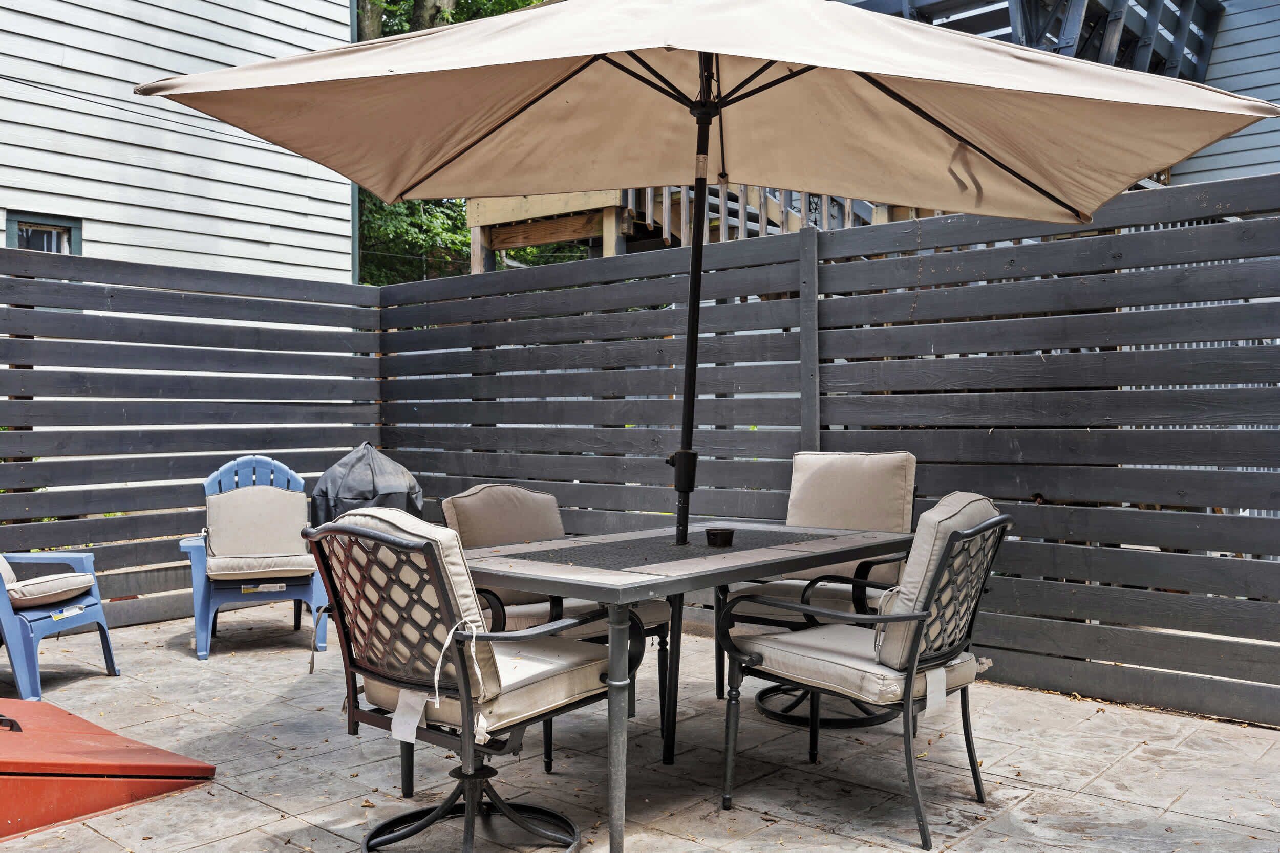 En udendørs terrasse med et bord, stole og en stor parasol, samt et træhegn.