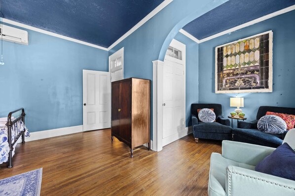 A room with a wooden floor, a dark blue wall, a white door, a dark wooden cabinet, and a blue sofa with decorative pillows.