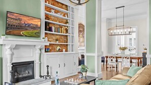 Ein Wohnzimmer mit Kamin, Bücherregal, Fernseher, Essbereich und einer Chandelier.