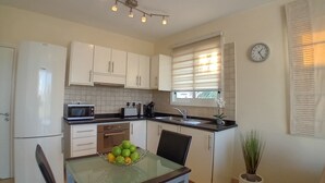 Une cuisine compacte avec des meubles blancs, un four à micro-ondes, un évier et un coin repas comprenant une table et des chaises.