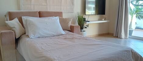 A bedroom with a bed, a TV, a plant, and a window with curtains.