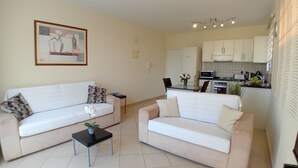 Un salon avec deux canapés, une petite table et une cuisine en arrière-plan.