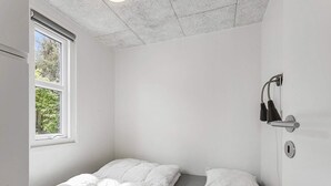 A small, white, single-bed room with a window, a wall-mounted light, and a door lock. - 4 Person Holiday Park Home in Skagen (Skagen)