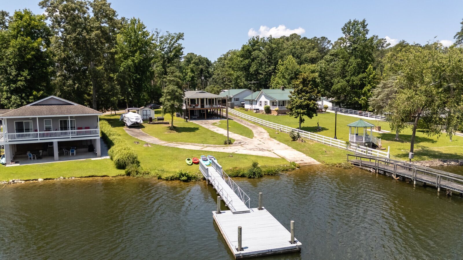 A lakeside property with a dock extending into the water, surrounded by lush greenery and multiple buildings.