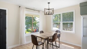 Un comedor con mesa y sillas, una araña y ventanas amplias con cortinas.