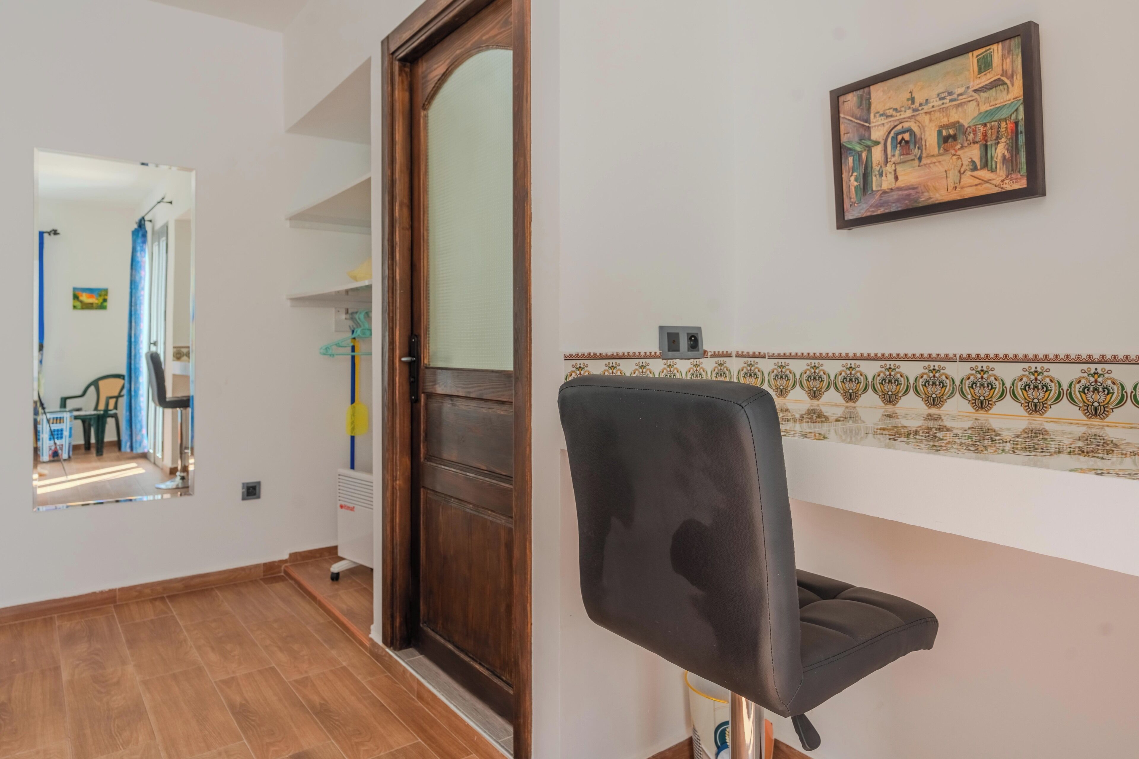 A room with a wooden door, a black office chair, a tiled backsplash, and a framed picture on the wall.