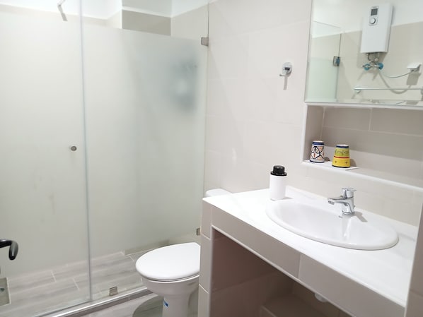 Un baño moderno con cabina de ducha de vidrio, inodoro blanco y lavamanos con espejo.