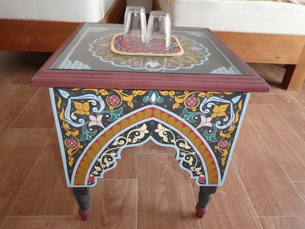A small, square table with a glass top and a colorful, ornate base.