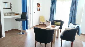A living room with a dining table, two black chairs, a yellow chair, and a sofa with a blue blanket.