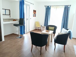 Una sala de estar con una mesa de comedor, dos sillas negras, una silla amarilla y un sofá con una manta azul.