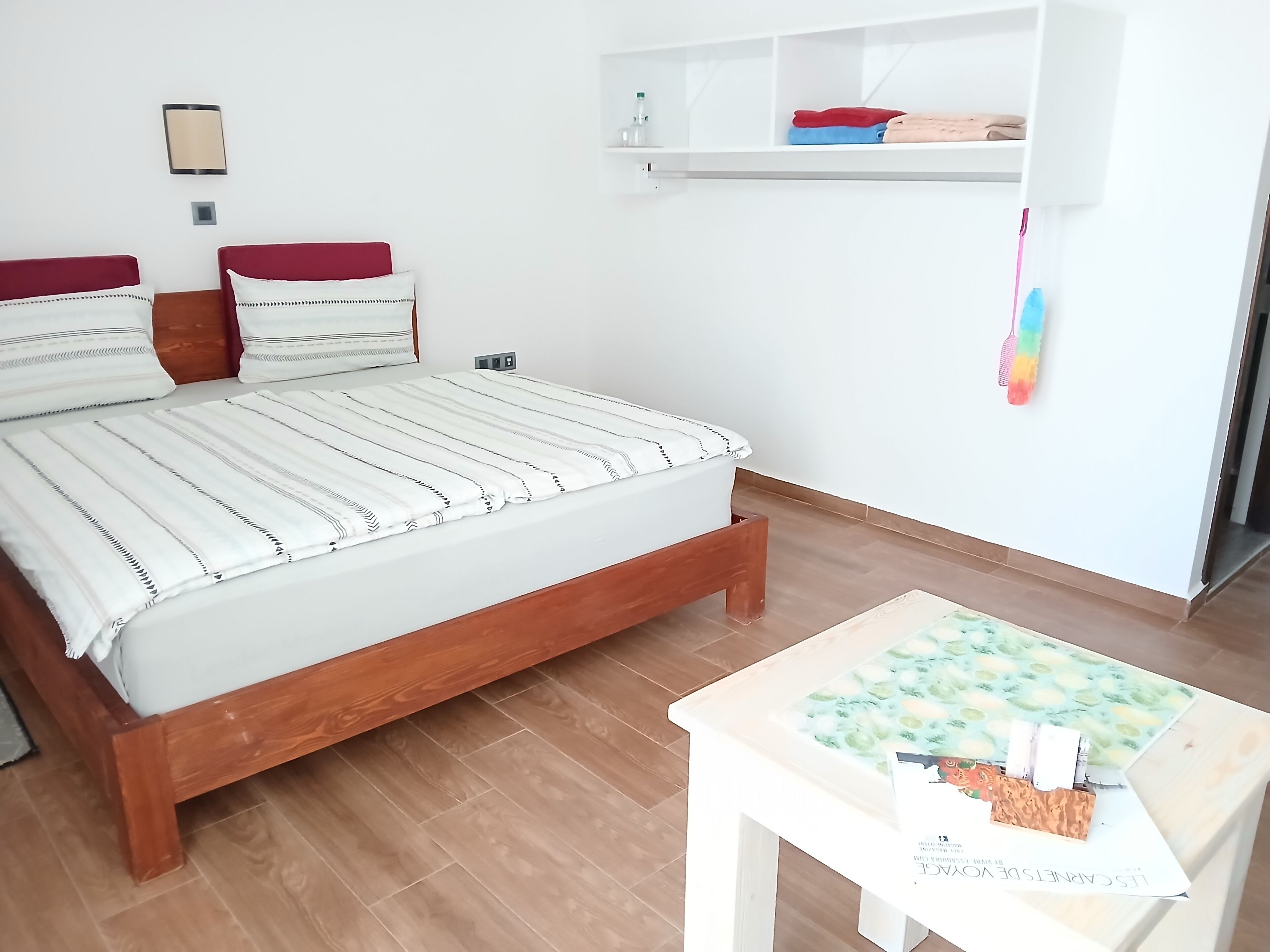 Une pièce comprenant un lit, une petite table et une étagère avec des vêtements pliés.