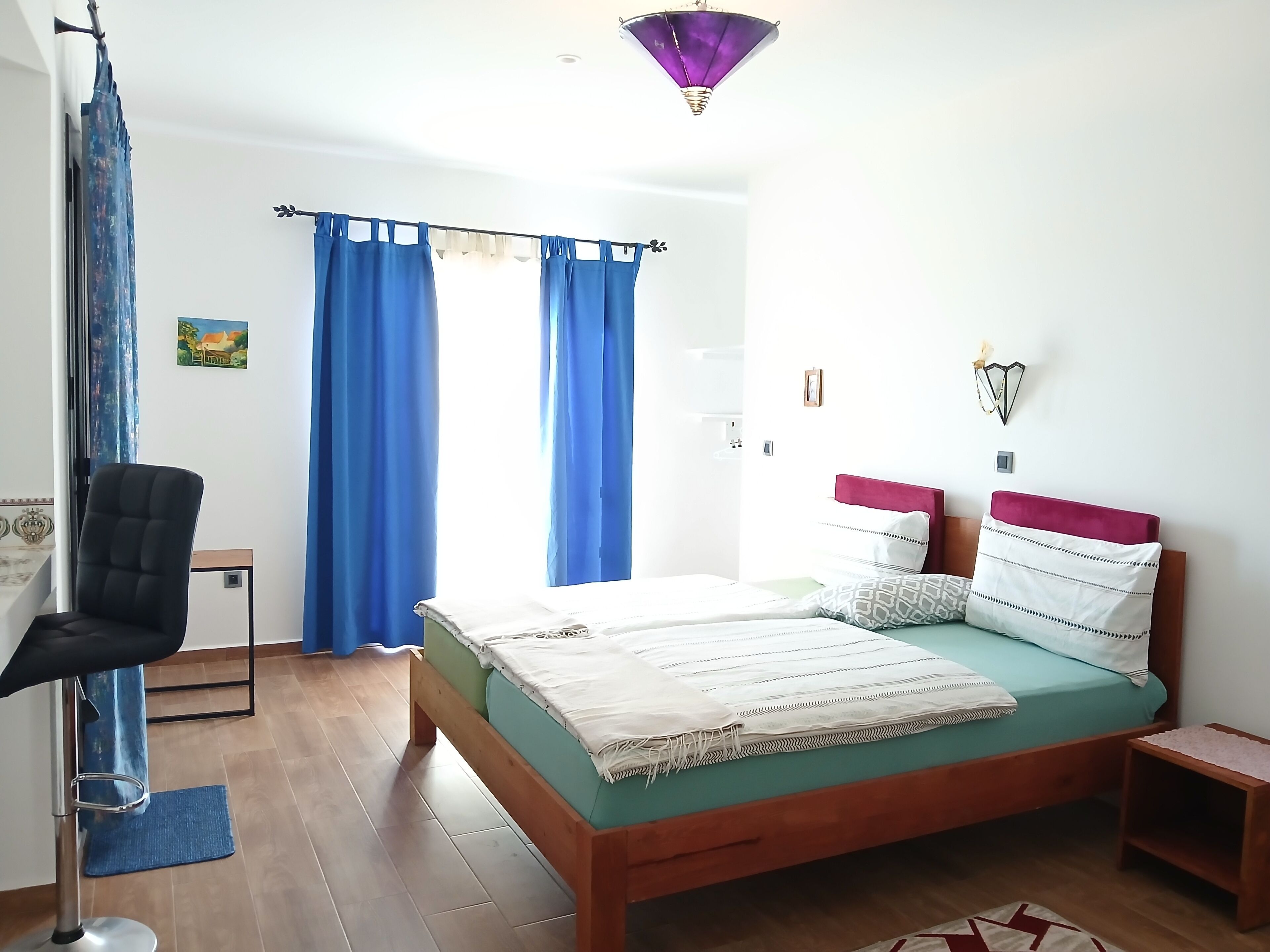 Un dormitorio con una cama, una silla, una mesita pequeña y una lámpara fijada a la pared.
